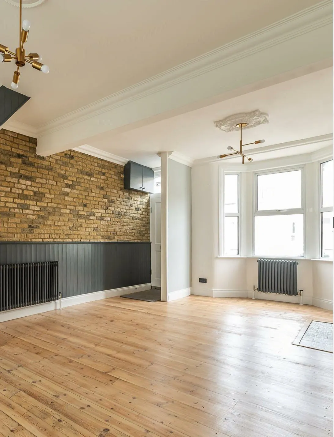 Bright open-plan living room with restored exposed brick wall, original floorboards and period cornicing