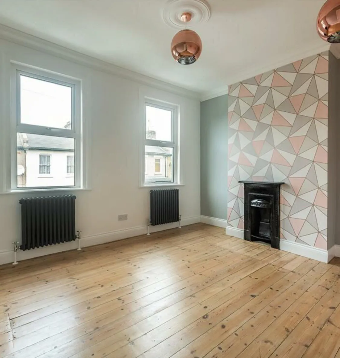 Bedroom with geometric wallpaper, copper pendants and Victorian fireplace